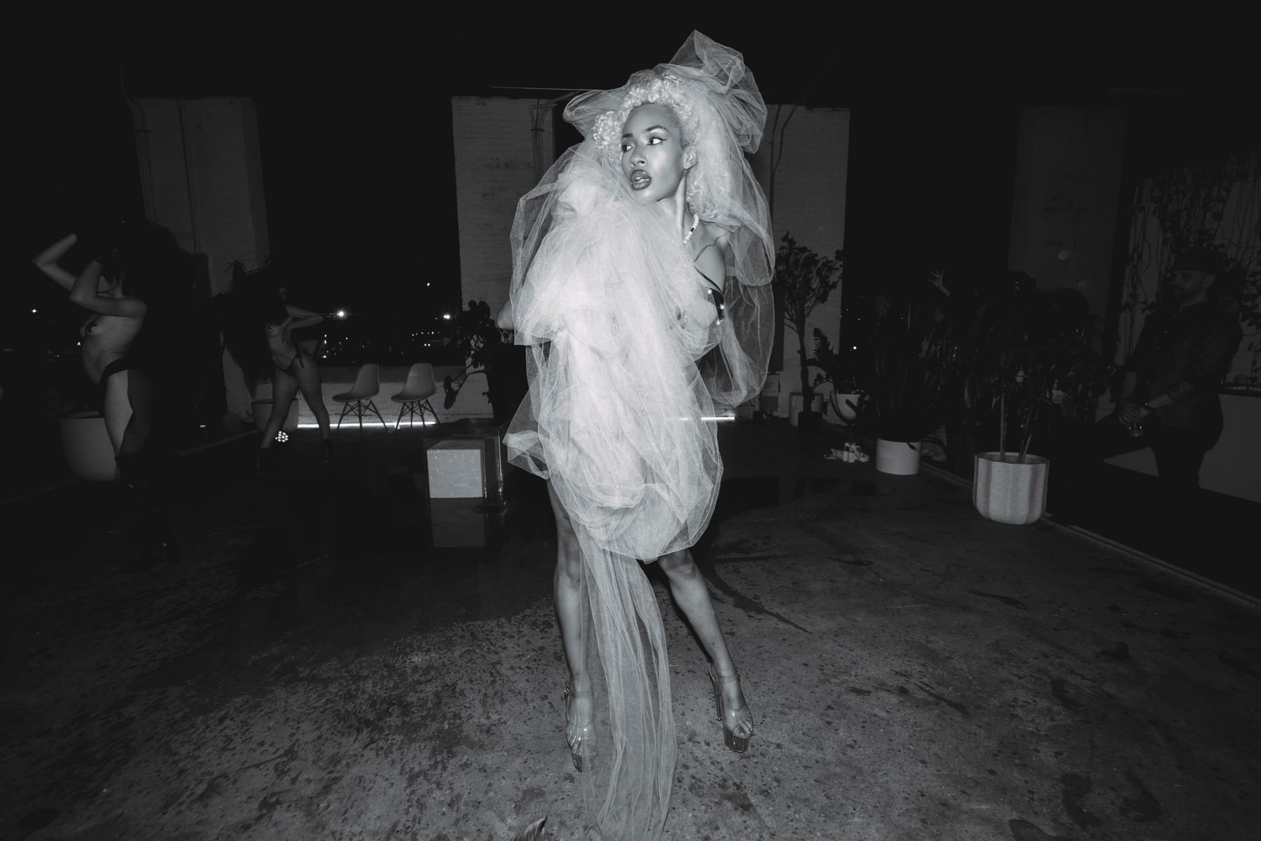 A woman wrapped in clouds of white tulle and a tulle headpiece in a loft above the city lights.