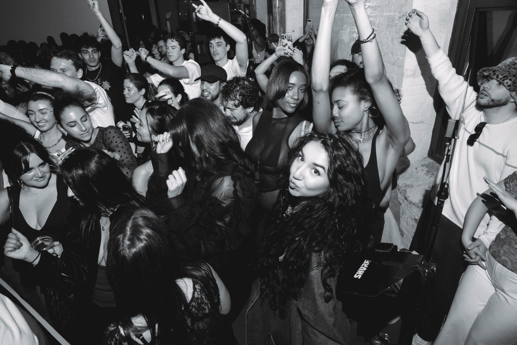 A dense, dancing crowd with arms raised; a woman in the foreground looks back at the camera.