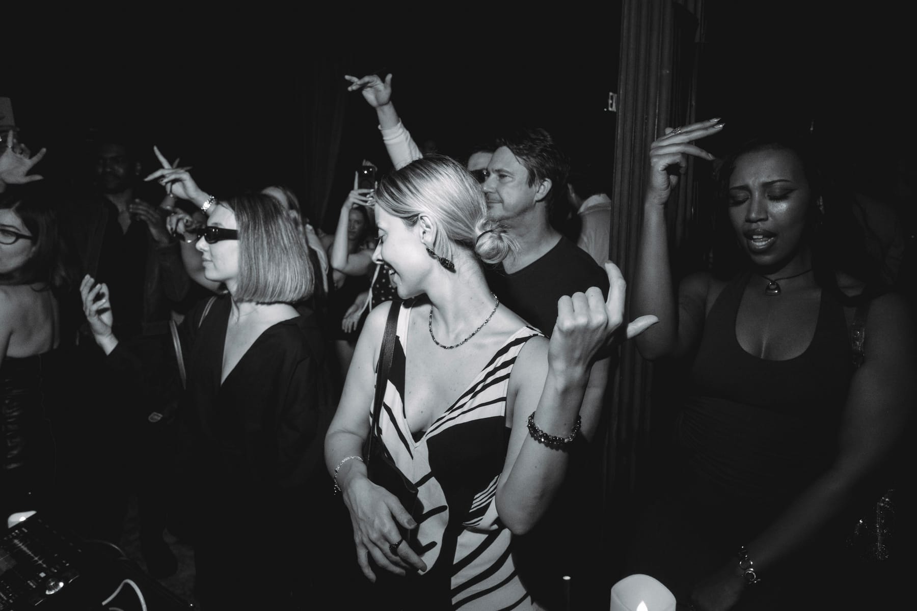 A woman in a striped dress dancing and smiling among a crowd with hands in the air.